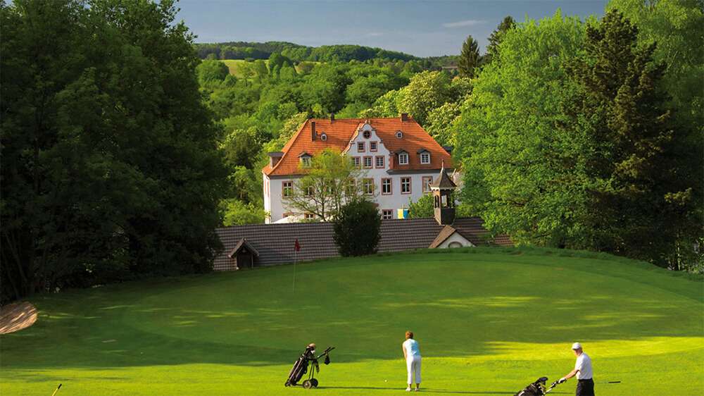 Bild des Schlosses Georghausen und einem Golfplatz mit Spielern im Vordergrund